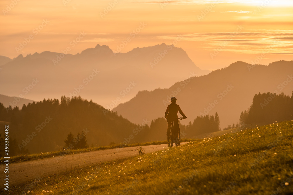 Fototapeta premium active woman riding her electric mountain bike at sunset in front of the awesome silhouette of Mount Saentis, Appenzell switzerland