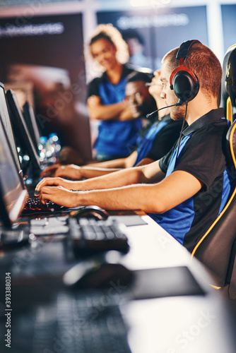 Professional cybersport gamers wearing headphones sitting in a row participating in eSport tournament, focus on a caucasian guy