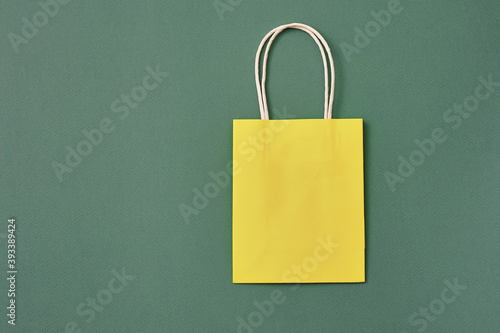 Gift yellow paper bag on a dark green background. Copy space, flat lay, mock up, top view