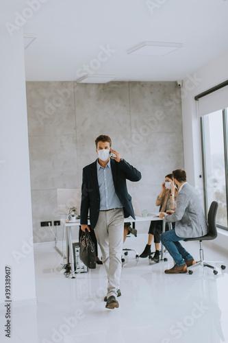 Young business man walking and using mobile phone while wear protective masks to prevent  corona viruus at office space photo