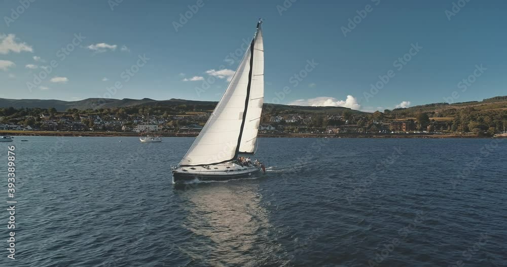 Regatta yacht sailing at pier town cityscape aerial. Sail boat cruise at open sea. Arran Island harbor with mountain shore. Passenger ship at ocean. Epic seascape at summer. Scotland, Europe Regatta yacht sailing at pier town cityscape aerial. Sail boat cruise at open sea. Arran Island harbor with mountain shore. Passenger ship at ocean. Epic seascape at summer. Scotland, Europe