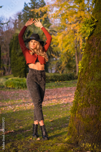 Lifestyle, blonde Caucasian girl in a red sweater and a black hat, enjoying nature in a park with trees in beautiful autumn, portrait of the young model smiling © unai