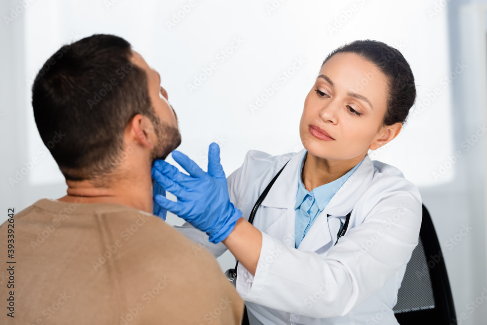 African american doctor in latex gloves examining neck of patient, sitting at office chair African american doctor in latex gloves examining neck of patient, sitting at office chair