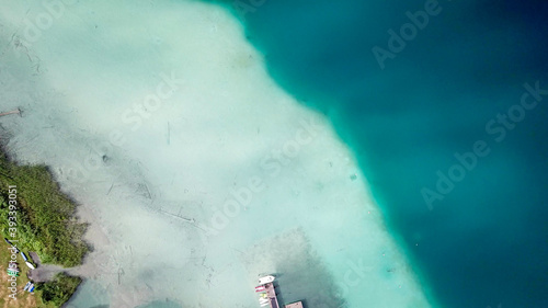 A top down, drone capture of Weissensee lake in Austrian Alps. The water changes color from white, turquoise to navy blue. Green shore of the lake. A bit of overcast. Serenity and peacefulness photo