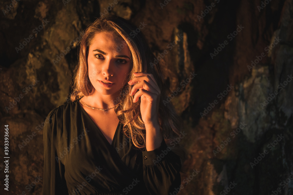 Obraz premium Lifestyle, a young Caucasian blonde in a black dress in a photo inside a cave, illuminated with yellow light. Very seductive pose of the model