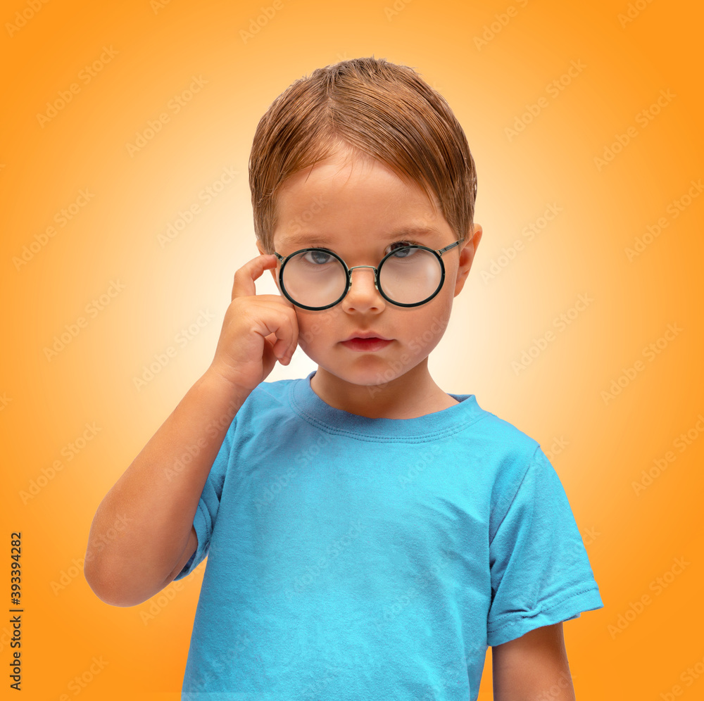 A little boy with glasses stands on an orange background
