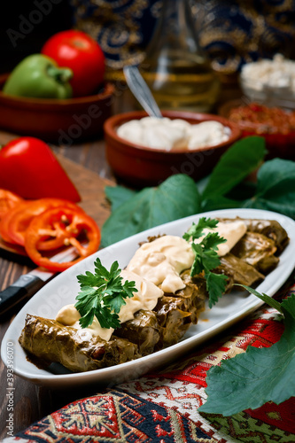 Mediterranean cuisine - dolma in plate with fresh cilantro and sauce on dark wooden table, close-up side view. Dolma, traditional dish of meat and grape leaves - Caucasian, Turkish and Greek cuisine