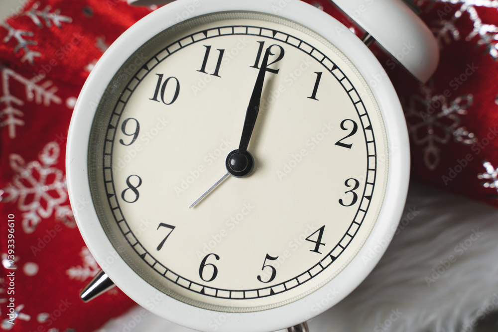 White alarm clock lying on the background of a red christmas hat White alarm clock lying on the background of a red christmas hat