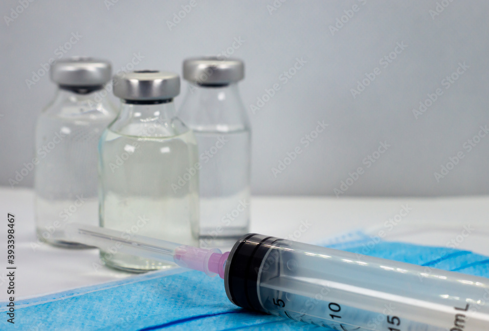 Vaccine Vial, Syringe and blue Medical Face Mask Vaccine Vial, Syringe and blue Medical Face Mask