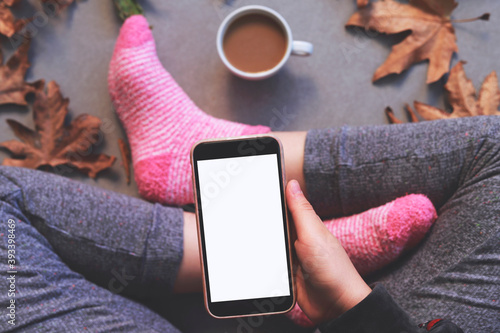 A woman in warm knitted socks is holding a telephone in her hands, next is a coffee cup. Autumn morning coffee.