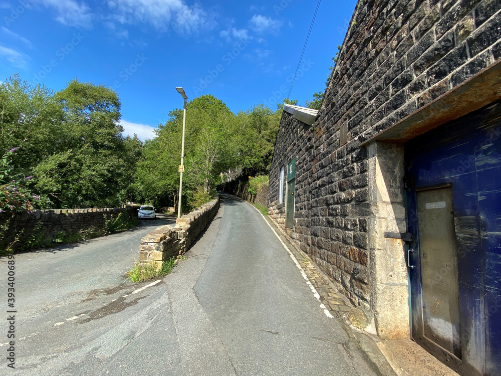 View up, Pudsey Lane, with stone buildings, and trees in, Cornholme, Todmorden, UK