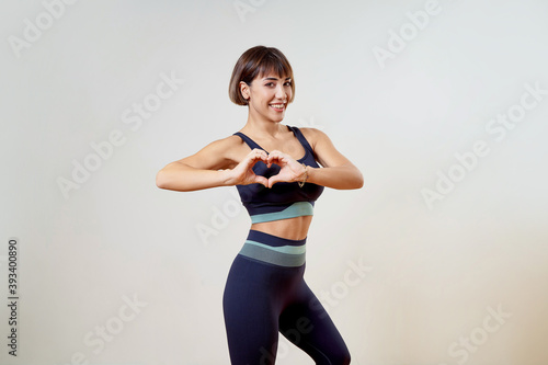 Attractive woman posing in front of a white background with navy blue yoga leggings and a sports tank top. Beautiful brunette sportswoman poses in front of a white background.