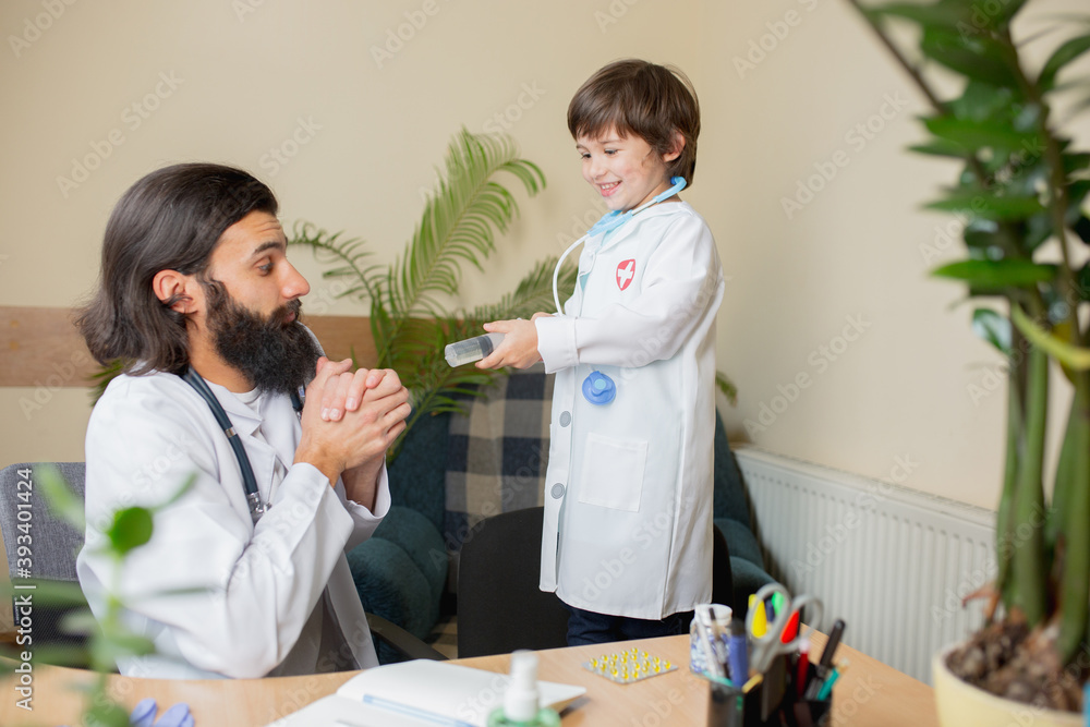 Paediatrician doctor examining a child in comfortabe medical office. Healthcare, childhood, medicine, protection and prevention concept. Little boy trust to doctor. Having fun while taking medicine