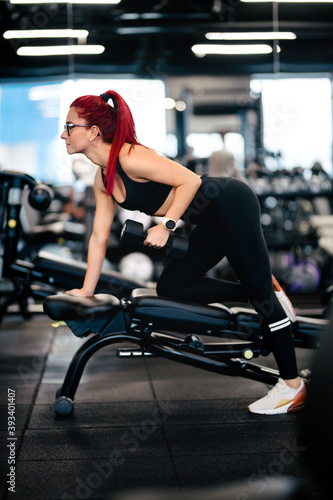 Attractive woman working out in the gym doing back exercises with dumbbells and staying healthy