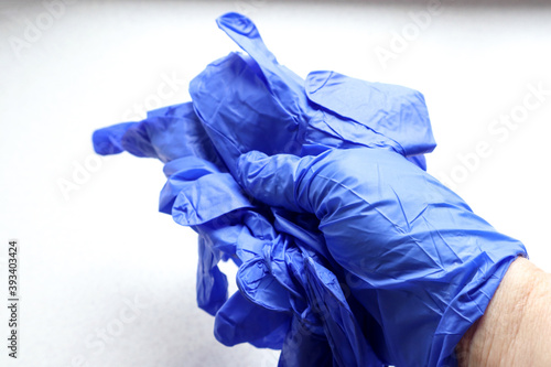 A hand in a blue glove holds protective gloves on a light background, close - up-the concept of compliance with the rules of disinfection