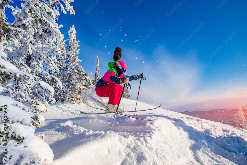 Woman skier jumping in pink skis on background of blue sky and snowy forest in mountains, dust from snow