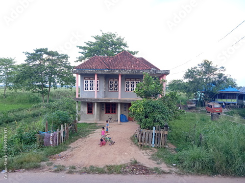 A two-story stone house in a remote village with lots of grass and red earth where young children play