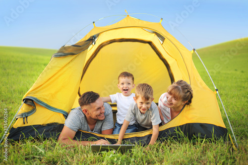 Cheerful family lying in a yellow tent and using their laptop  © mrkotov