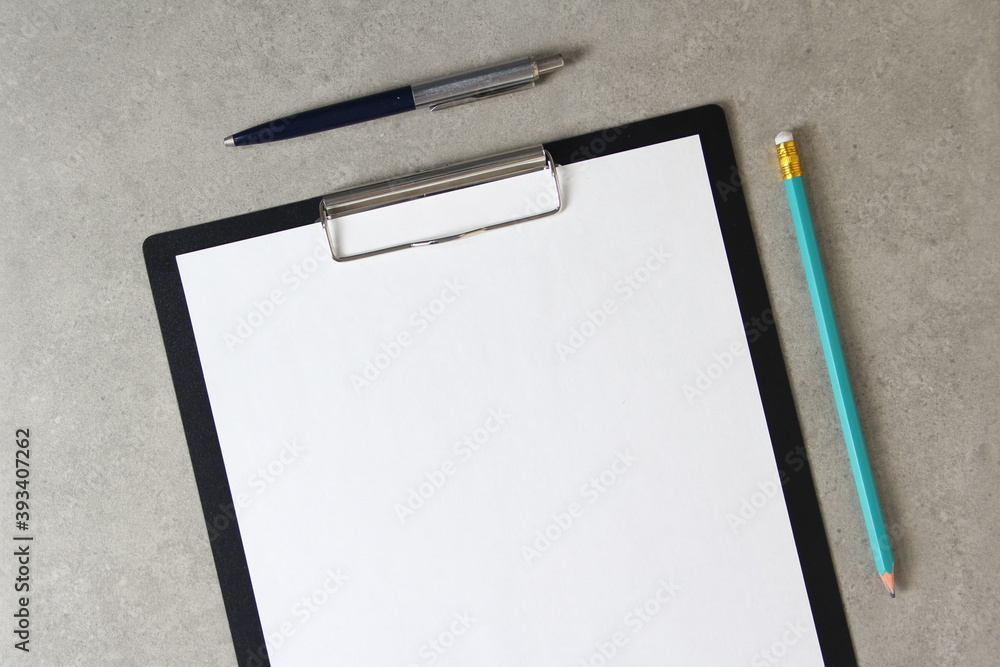 Template of white paper with a ballpoint pen and simple pencil on light grey concrete background in a black tablet with a clip. Concept of new idea, business plan and strategy, empty space for text Template of white paper with a ballpoint pen and simple pencil on light grey concrete background in a black tablet with a clip. Concept of new idea, business plan and strategy, empty space for text