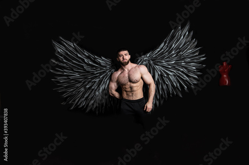 handsome muscular man in angel costume with black wings on black background