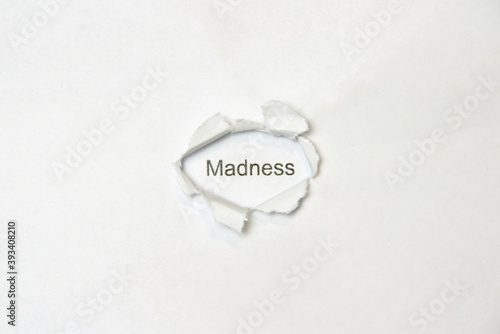 Word Madness on white isolated background through the wound hole in the paper.