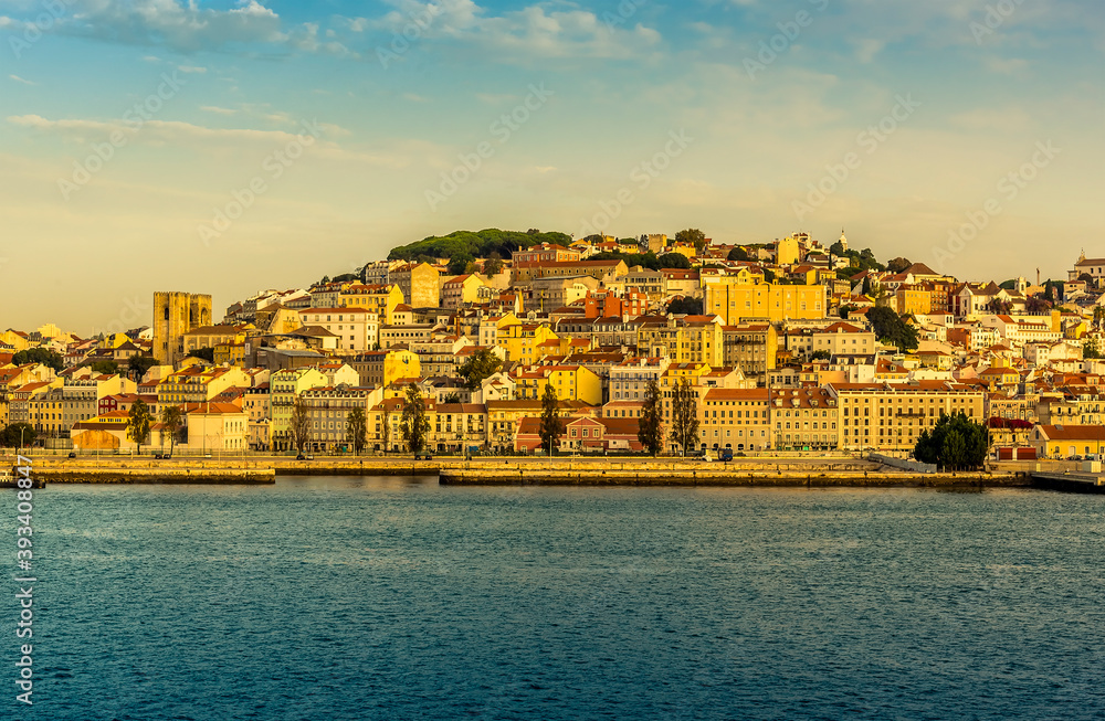 The old quarter and castle district of Lisbon, Portugal viewed from the river Tagus bathed in the early morning light at sunrise in Autumn