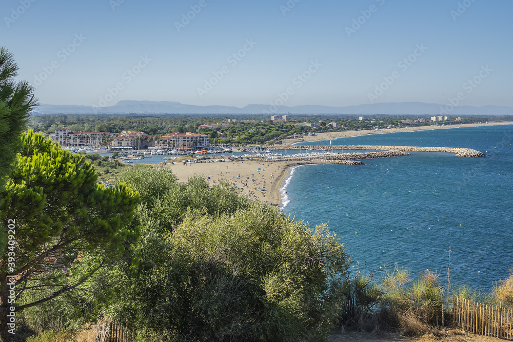 Sandy Mediterranean beach Le Racou in Argeles sur Mer with its old fishermens houses and the harbor in background, Roussillon, Pyrenees Orientales, France.