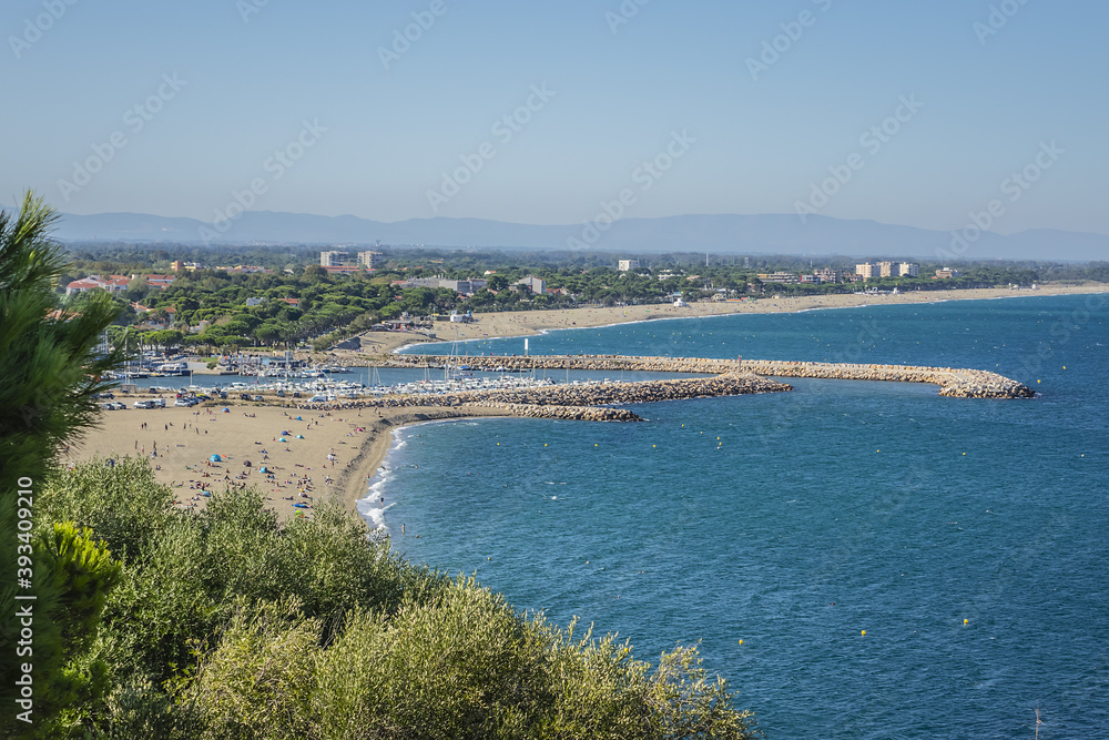 Sandy Mediterranean beach Le Racou in Argeles sur Mer with its old fishermens houses and the harbor in background, Roussillon, Pyrenees Orientales, France.