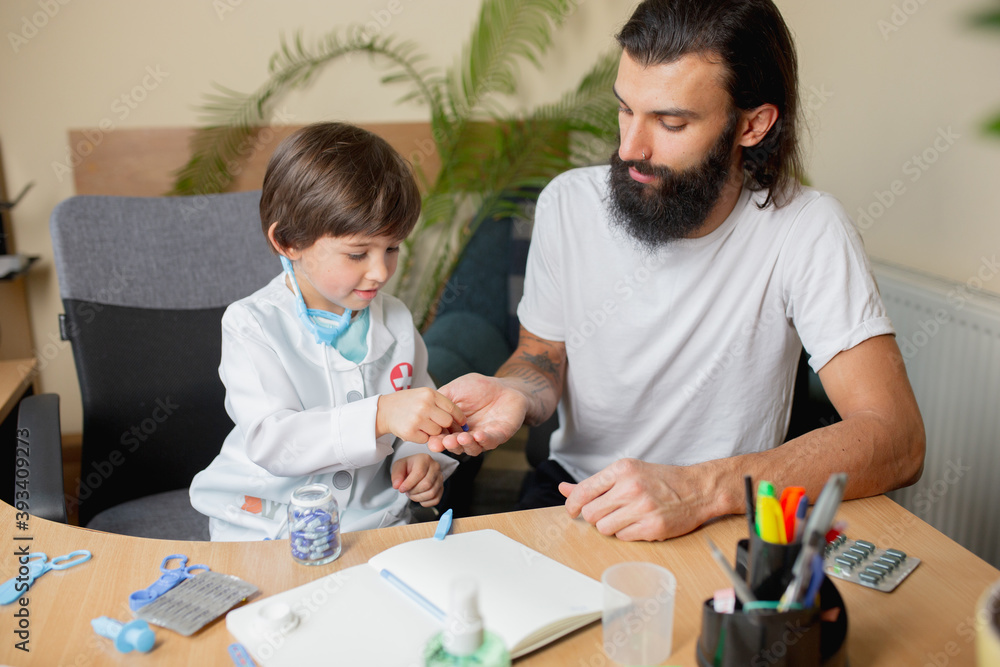 Little boy playing pretends like doctor examining a man in comfortabe medical office. Healthcare, childhood, medicine, protection and happiness concept. Having fun, laughting while giving pills Little boy playing pretends like doctor examining a man in comfortabe medical office. Healthcare, childhood, medicine, protection and happiness concept. Having fun, laughting while giving pills