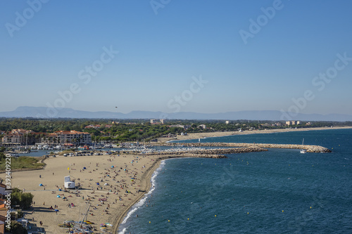 Sandy Mediterranean beach Le Racou in Argeles sur Mer with its old fishermens houses and the harbor in background, Roussillon, Pyrenees Orientales, France.