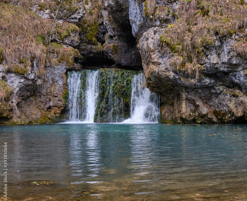 Fototapeta premium a small waterfall in the autumn forest flows out of the rock