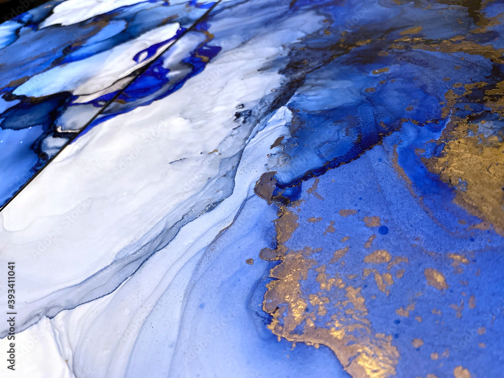 Abstract blue background with beautiful smudges and stains made with alcohol ink and gold pigment. Fragment of art with blue texture resembles watercolor or aquarelle painting.
