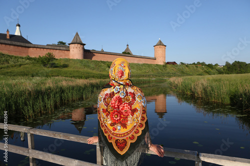 Summer in Russia. Russian tourist woman in traditional national Pavlovo Posad folk shawl, Pavloposadsky scarf. Kremlin in Suzdal town, Vladimir region, Russia. Summer travel in Russia. Kamenka river photo