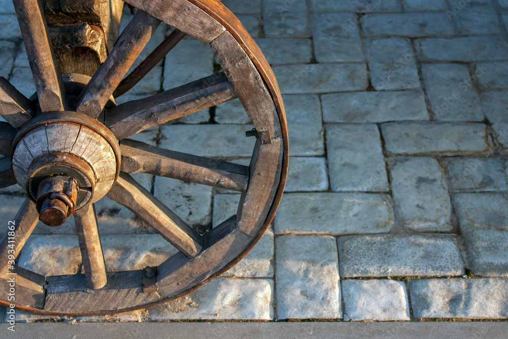 A wooden wheel covered with an iron hoop. The wheel of the cart is illuminated by the sun. Close-up, side view.