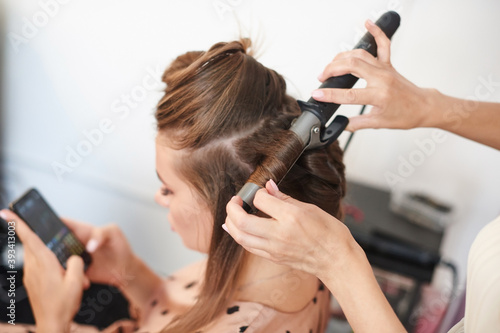 hairdresser hands with curling iron makes hair styling for young business woman