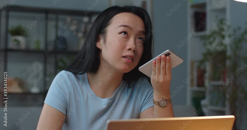 Close up portrait of Asian young woman recording voice message on smartphone sitting at table at office. Female professional speaking on cellphone indoor in cabinet. Employment concept Close up portrait of Asian young woman recording voice message on smartphone sitting at table at office. Female professional speaking on cellphone indoor in cabinet. Employment concept