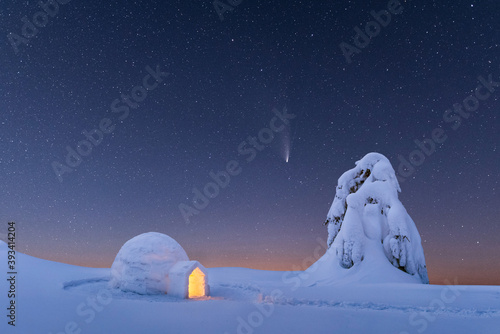 Snow igloo luminous from the inside in the winter mountains. Starry sky with comet on the background photo