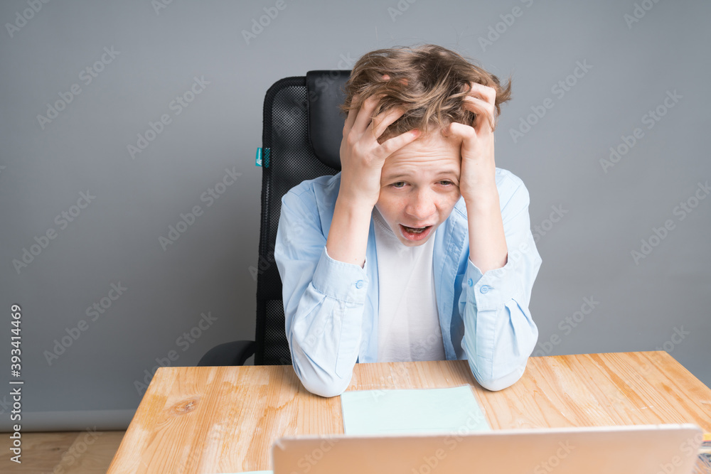 A schoolboy boy sits on an online lesson via a computer, holding his head. Homeschooling, tired of studying, coronavirus pandemic A schoolboy boy sits on an online lesson via a computer, holding his head. Homeschooling, tired of studying, coronavirus pandemic