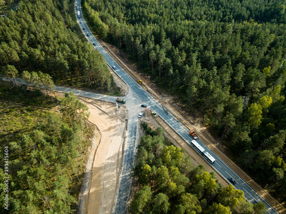 Aerial view of highway with cars and forest. Construction site of new way. Truck and road roller on sand.