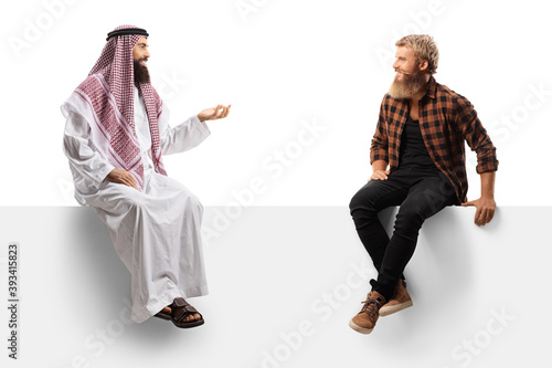 Arab man in a thobe and a bearded guy hipster seated on a panel talking photo