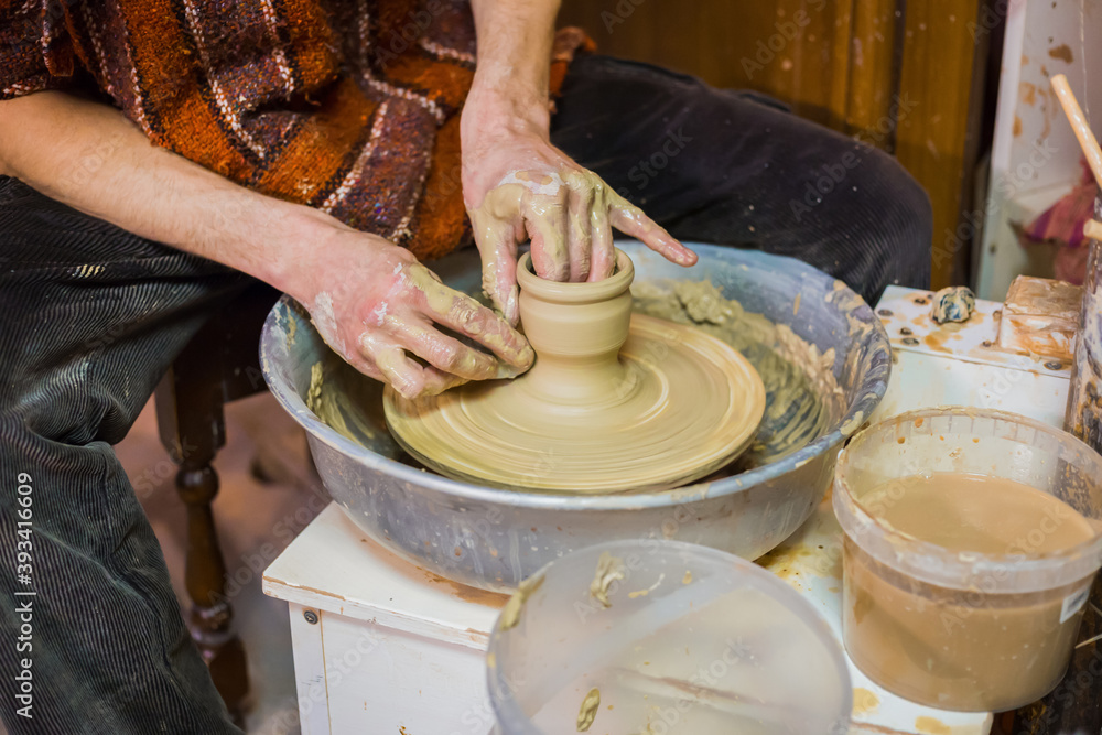 Professional male potter making ceramics on pottery wheel in workshop, studio. Close up view of potter hands. Handmade, art and handicraft concept