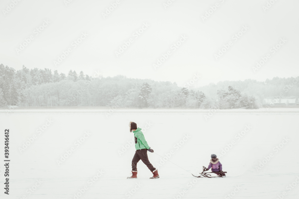 Parenthood, fatherhood fashion, season and people concept - happy family with children on sleds walking in winter outdoors on surface of frozen lake. Father pulling a sled at snow. Christmas vacation.