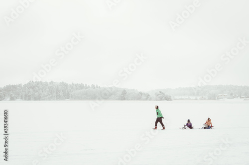Parenthood, fatherhood fashion, season and people concept - happy family with children on sleds walking in winter outdoors on surface of frozen lake. Father pulling a sled at snow. Christmas vacation.