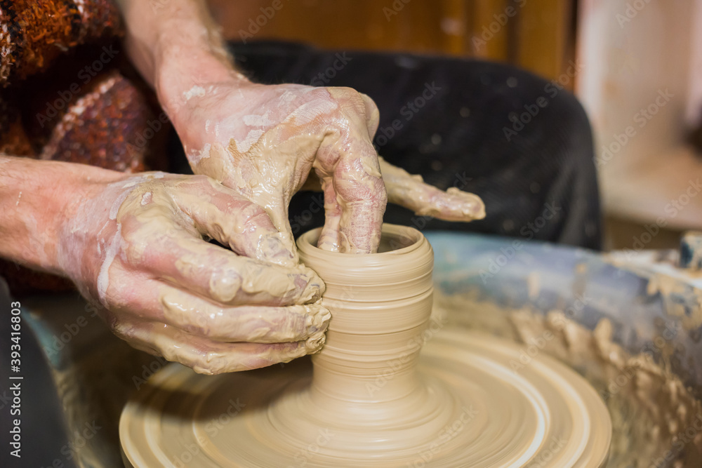 Close up view - professional male potter making clay cup on pottery wheel at workshop, studio. Handmade, art, handicraft concept
