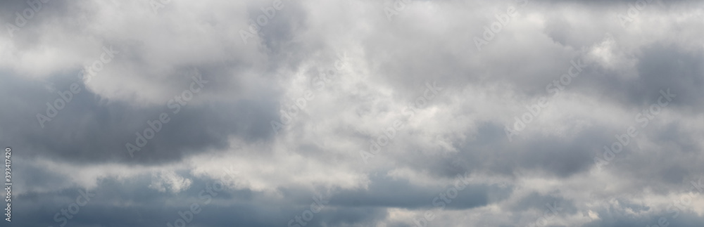 Cloudy sky with gray clouds and a light gap in the center, panorama of the sky