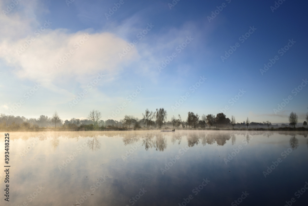 Landscape with a lake in autumn, over which the fog clears in the morning and the sun rises
