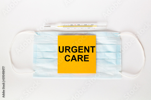 Sticker with text Urgent Care lying on the mask with a thermometer