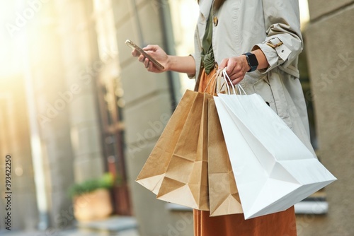 Texting sms to a friend. Cropped shot of a woman with shopping bags using her smartphone while standing on city street outdoors