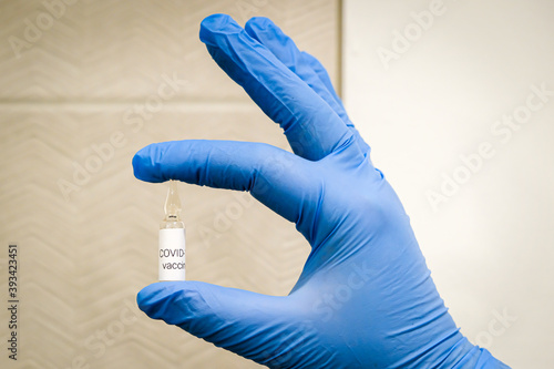 Hand in blue medical gloves holding small ampoule with label Covid-19 vaccine. Coronavirus covid 19 cure concept.