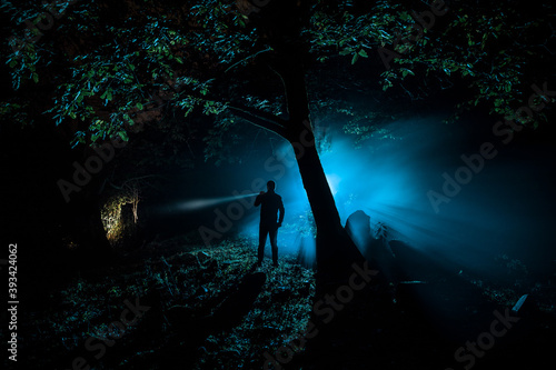 strange light in a dark forest at night. Silhouette of person standing in the dark forest with light. Horror halloween concept. strange silhouette in a dark spooky forest at night